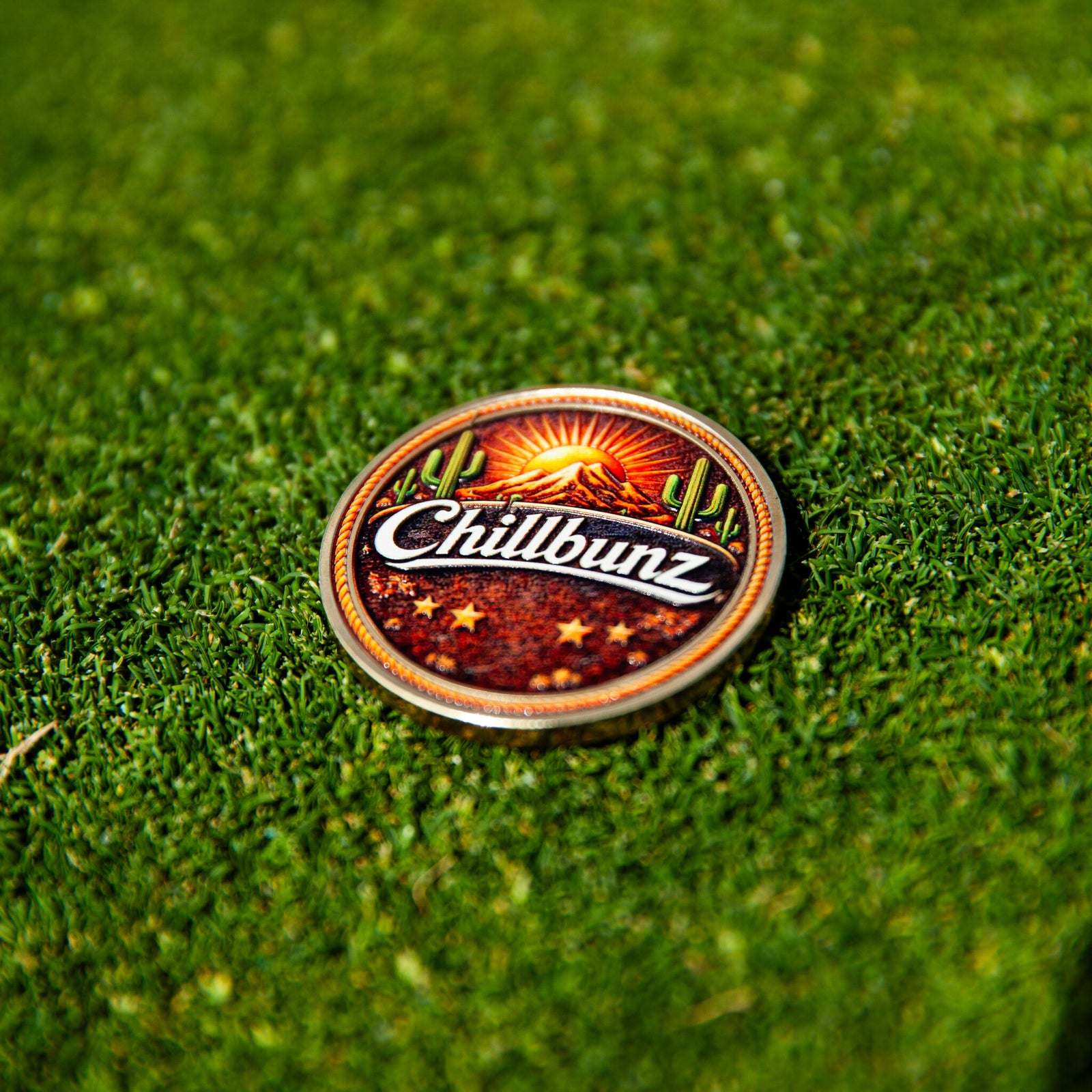 Desert Classic ball marker, cactus and sunset design, on the putting green beside a golf ball