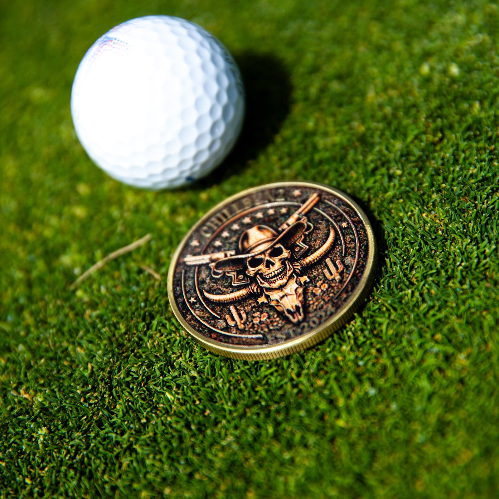 Outlaw Chill ball marker, metal horned skull design, on the green beside a golf ball