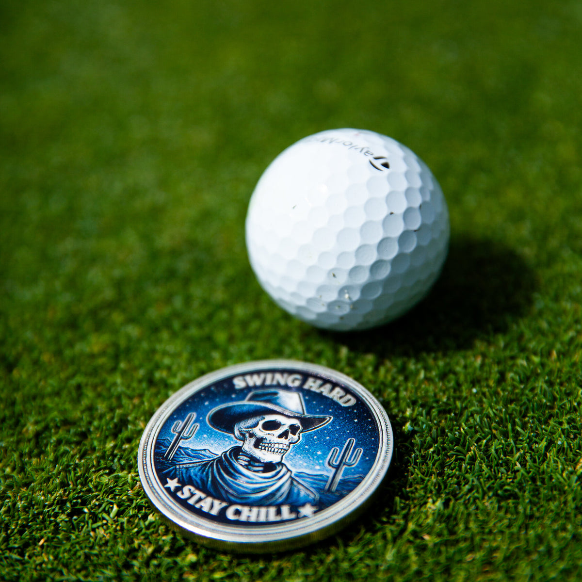 Swing Reaper ball marker, blue skull design, on the putting green beside a golf ball