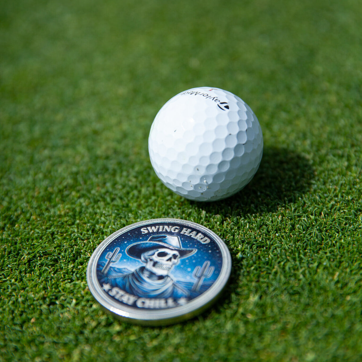 Swing Reaper ball marker, blue skull design, on the green beside a golf ball